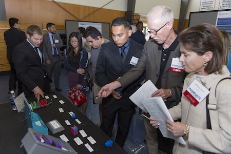 Two competition judges stand in front of a table at the spring 2017 Innovate to Grow as the students explain their projects to the judges.