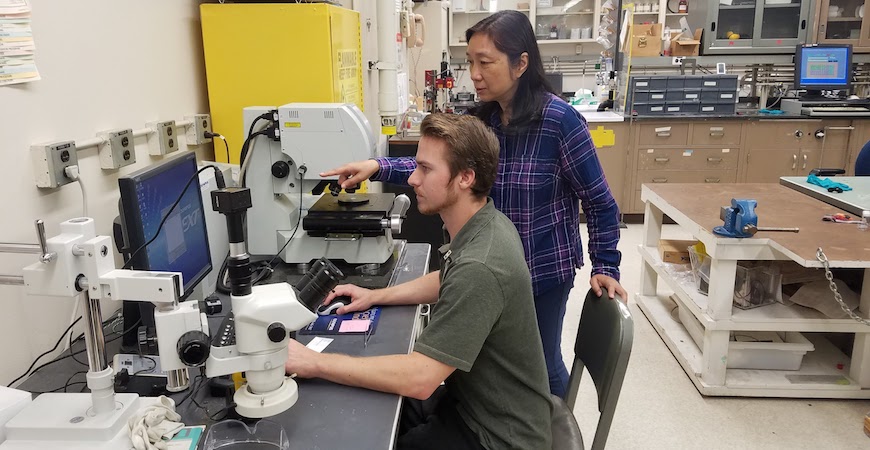 A student sitting at a computer with a NASA scientist standing behind him are working together in a laboratory.