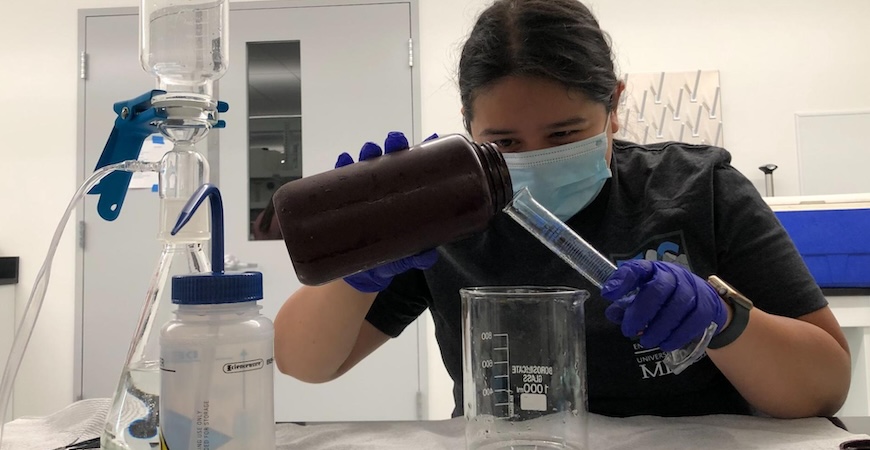 Photo depicts Brittany Barreto Martinez pouring liquid into a test tube in a lab.