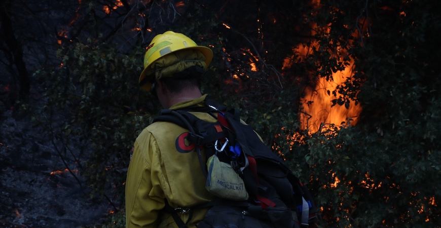 Photo depicts a firefighter and flames from the 2020 Apple fire in California.