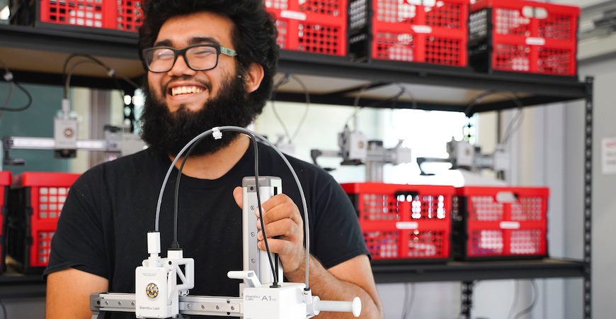 Photo depicts a UC Merced student holding a 3D printer available for use at the university's Makerspace.