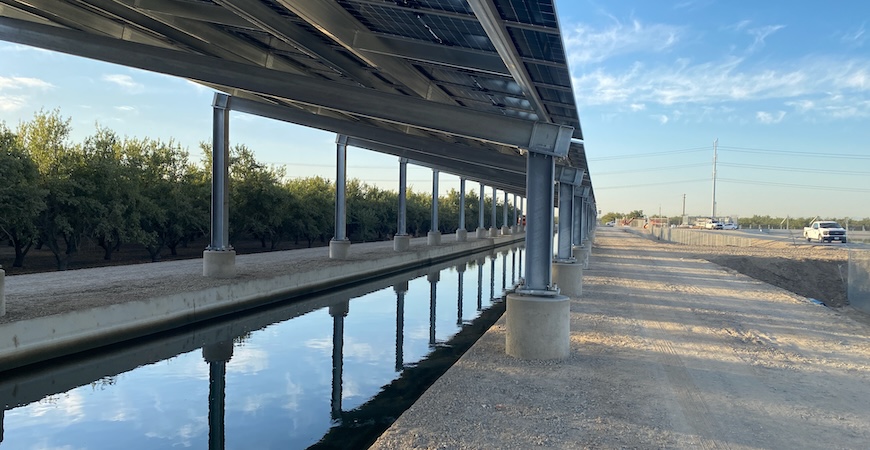 Photo depicts solar panels mounted on concrete supports over a canal.